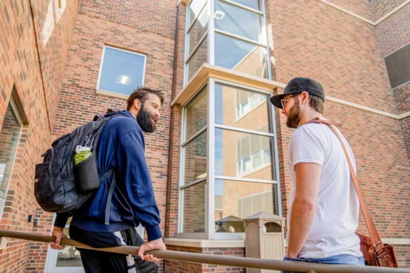 Two students standing and walking outside a campus building.