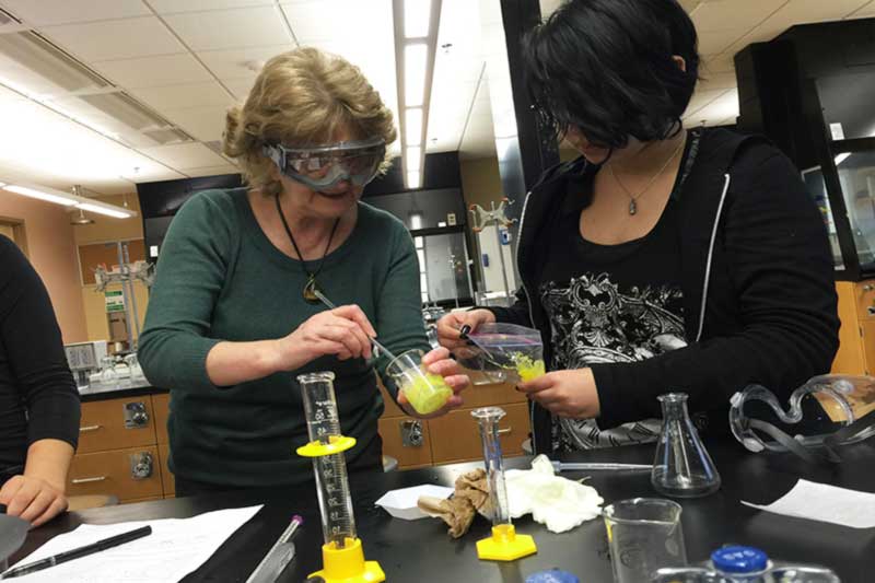 Instructor and students handling materials in a chemistry lab.