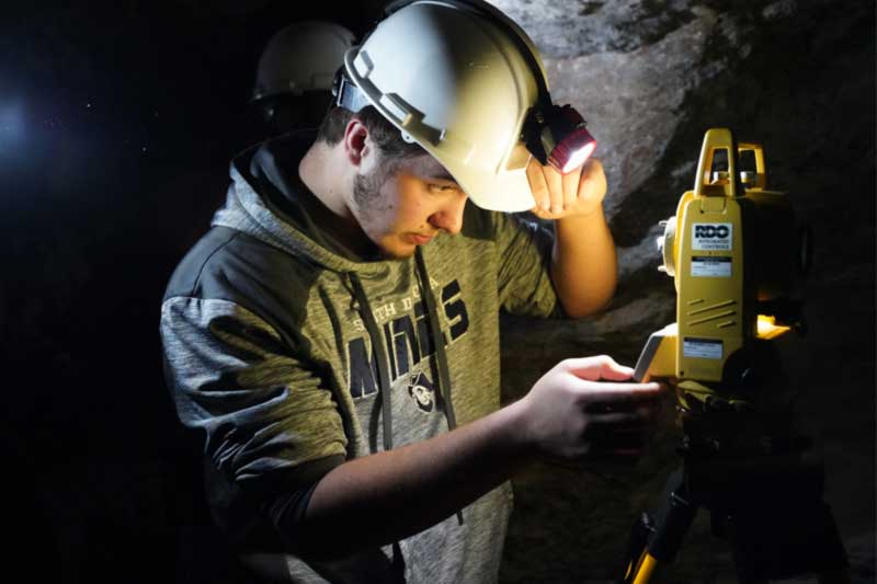 Student wearing a hard hat working in an underground mining environment.