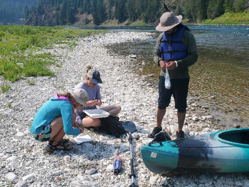 Students conducting field research alog a riverbank.