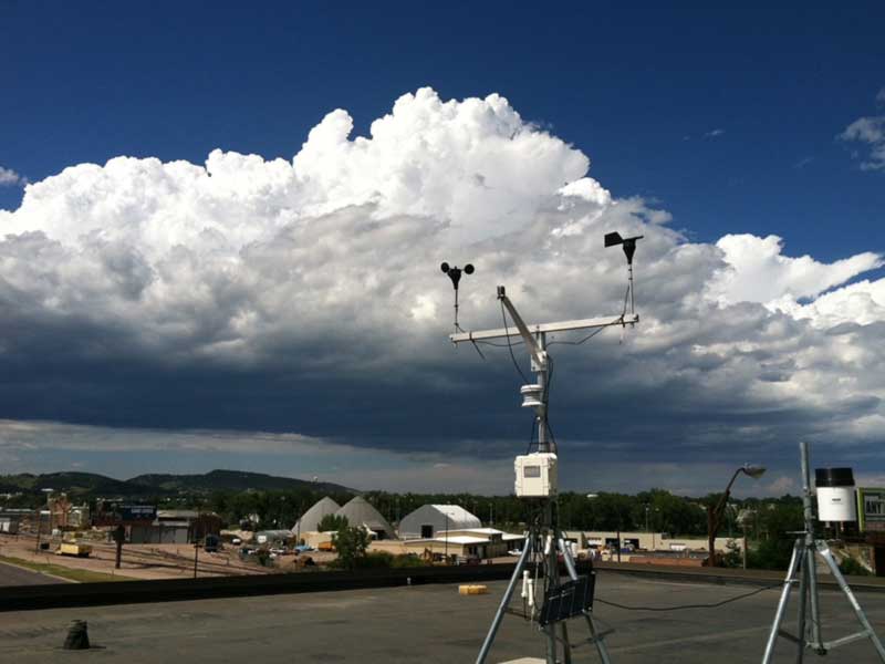 Meteorological instruments set up outdoors beneath large storm clouds.