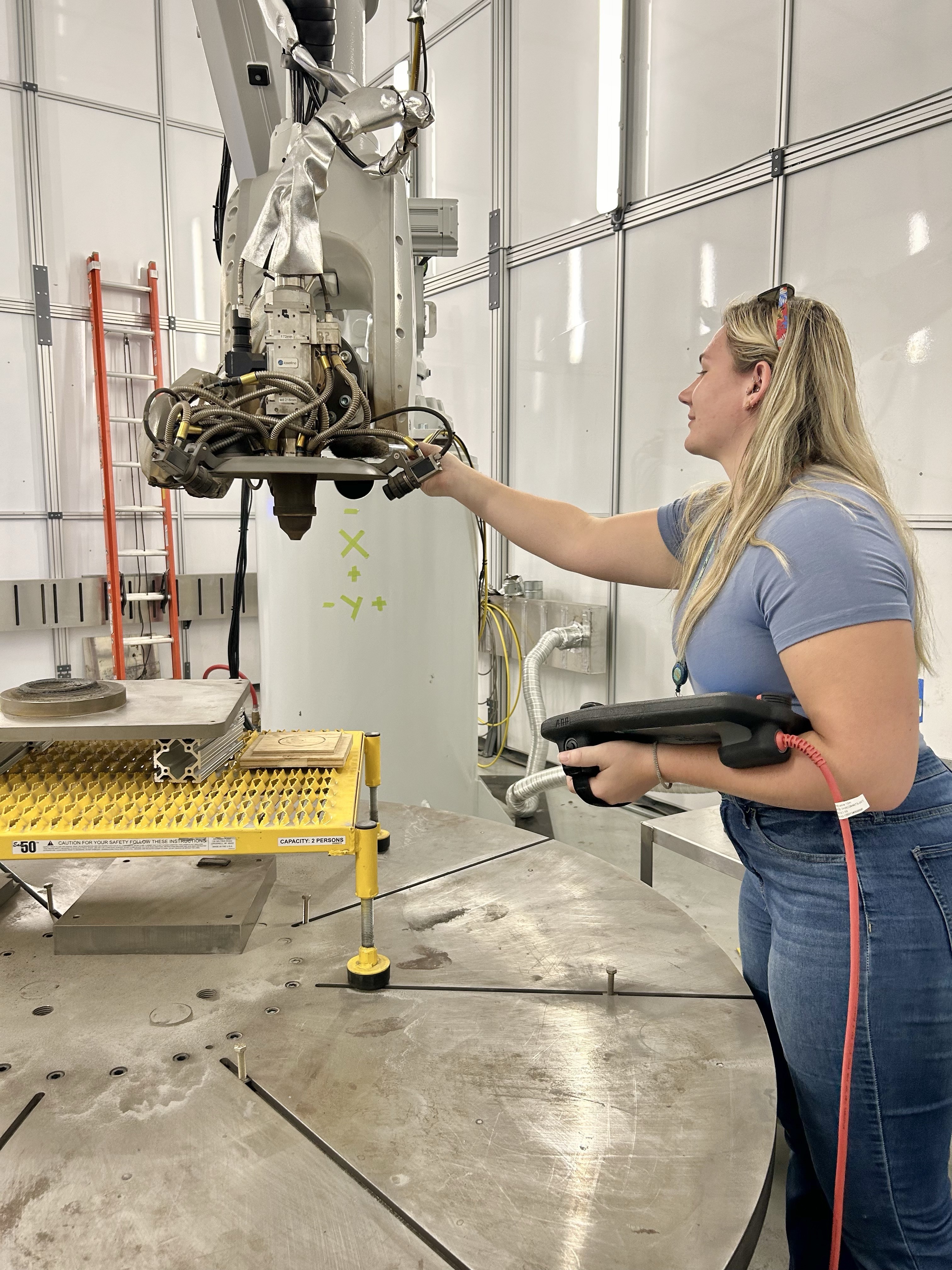 Jenna Sayler inspects the Directed Energy Deposition (DED) robot, a device used for additive manufacturing with metal powder, before performing some dry runs of the print. 